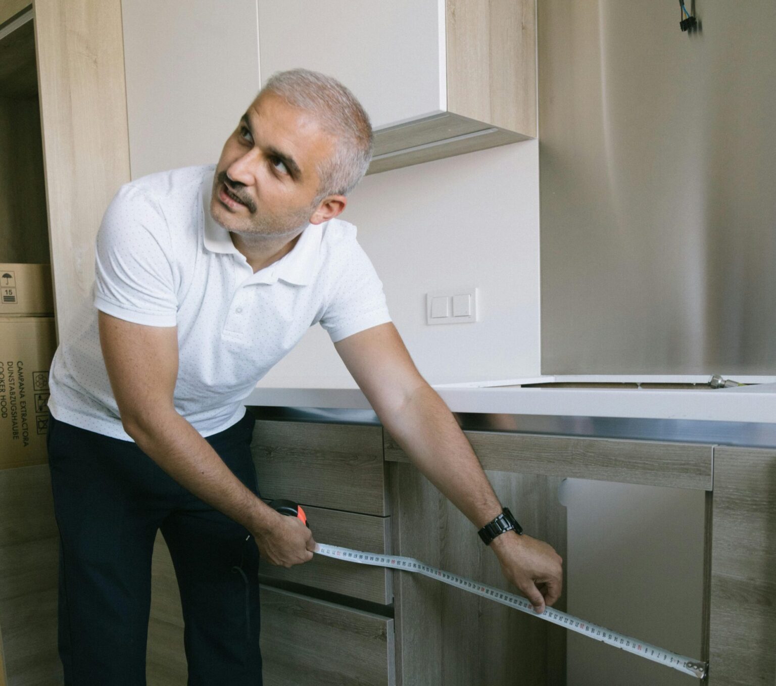 A man using a measuring tape to measure kitchen cabinets in a modern Istanbul apartment.