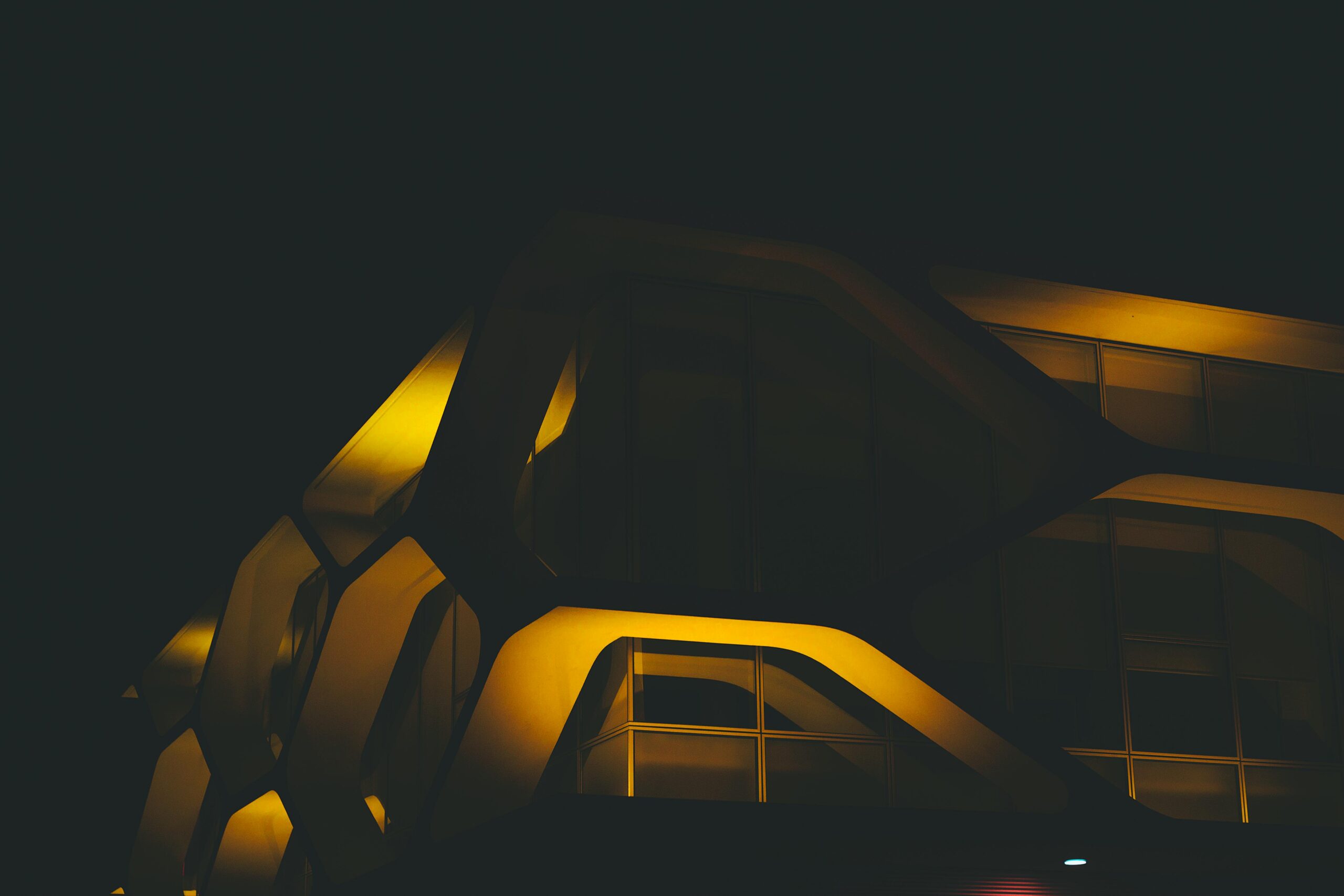 An illuminated modern building with futuristic design captured at night, featuring dramatic lighting.